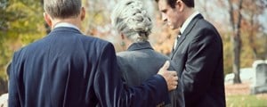 Woman being comforted by adult sons at a funeral