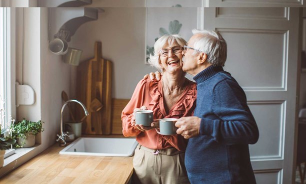 Older couple near kitchen sink, one kissing other on cheek
