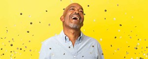 Man laughing in front of yellow wall with confetti
