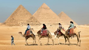 three people riding camels in front of the pyramids of giza